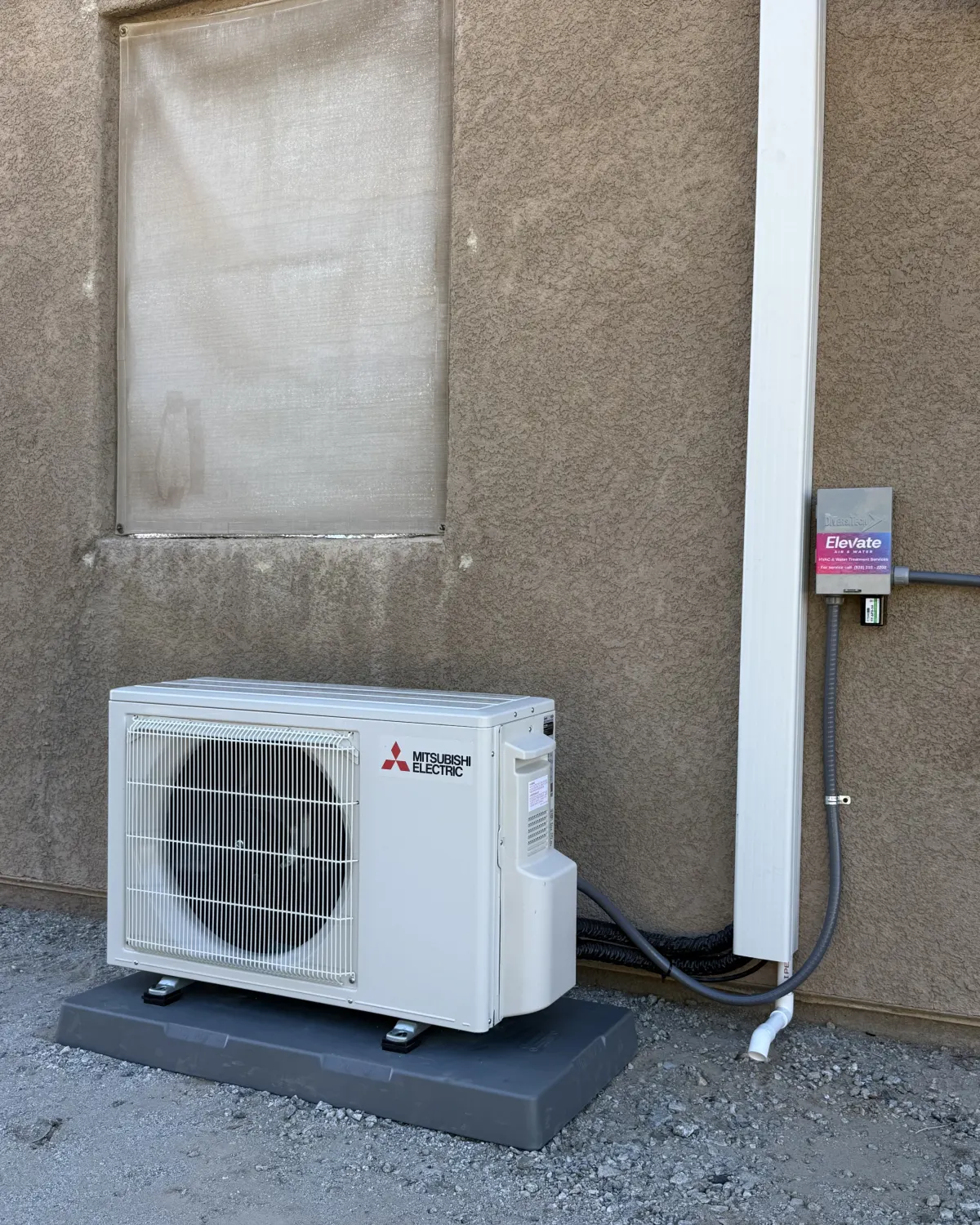 Ductless mini-split outdoor unit with an Elevate sticker on a stucco wall