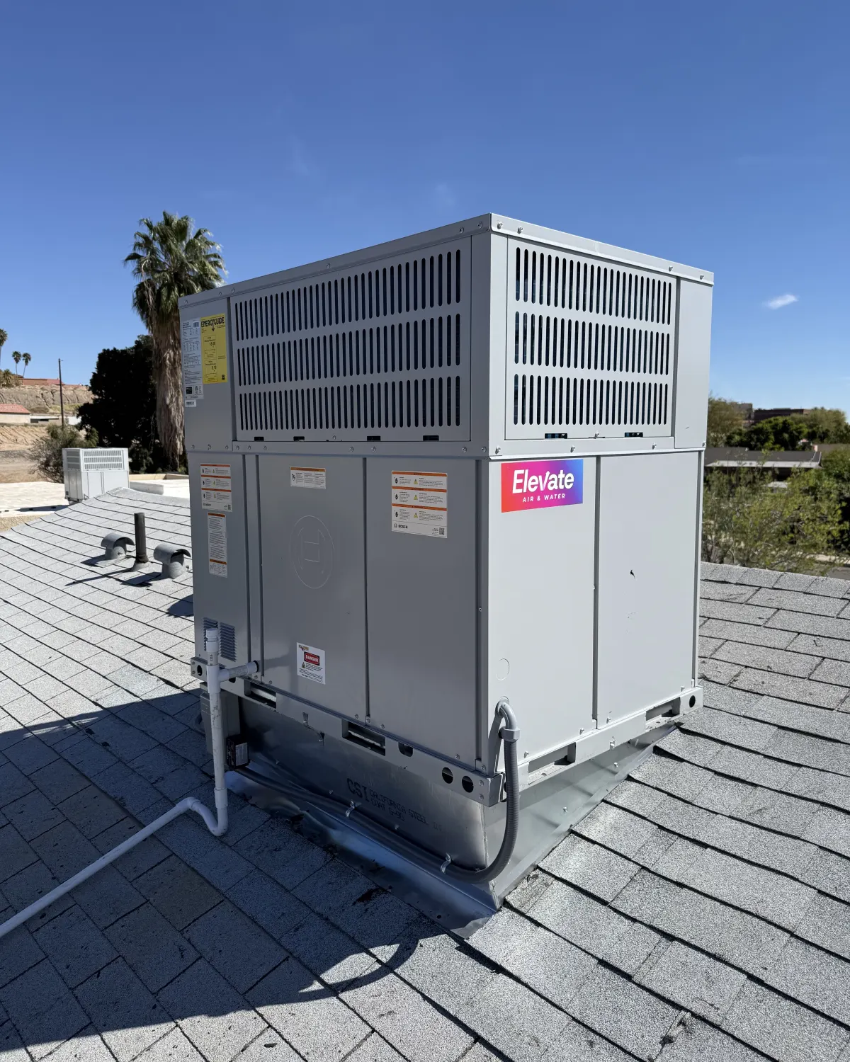 Rooftop HVAC unit with an Elevate sticker, palm trees and desert hills behind